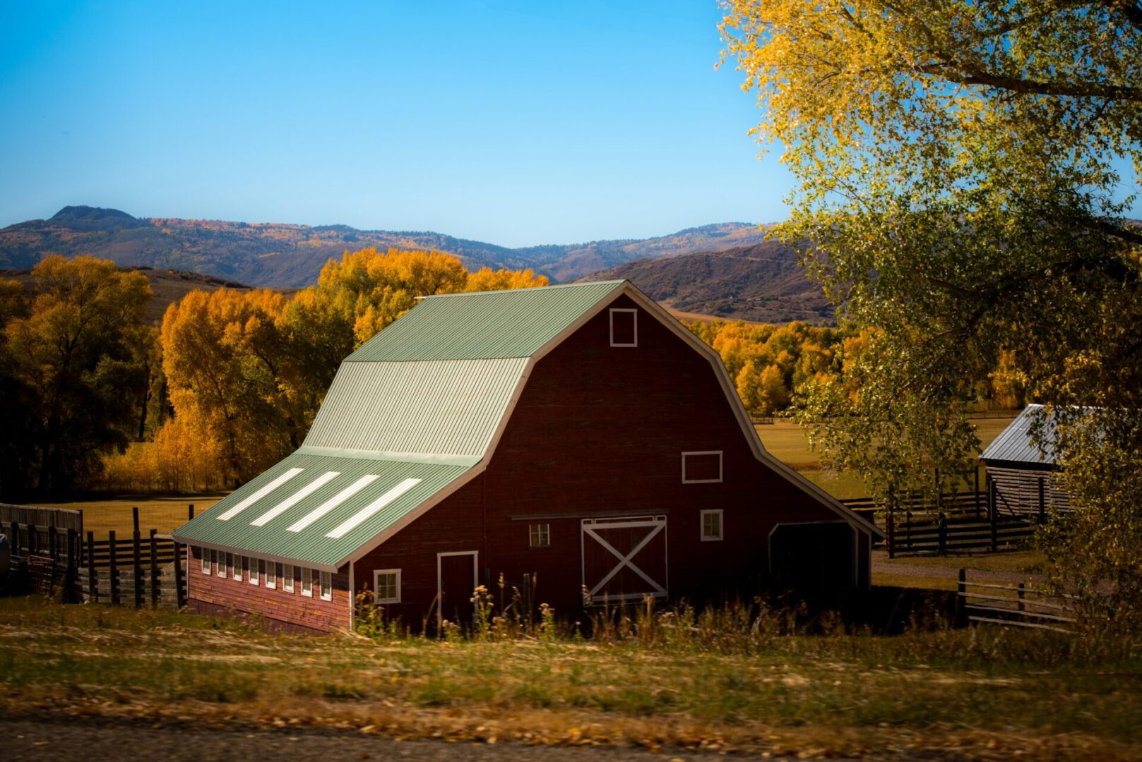 A red barn with green roof in the middle of a field.